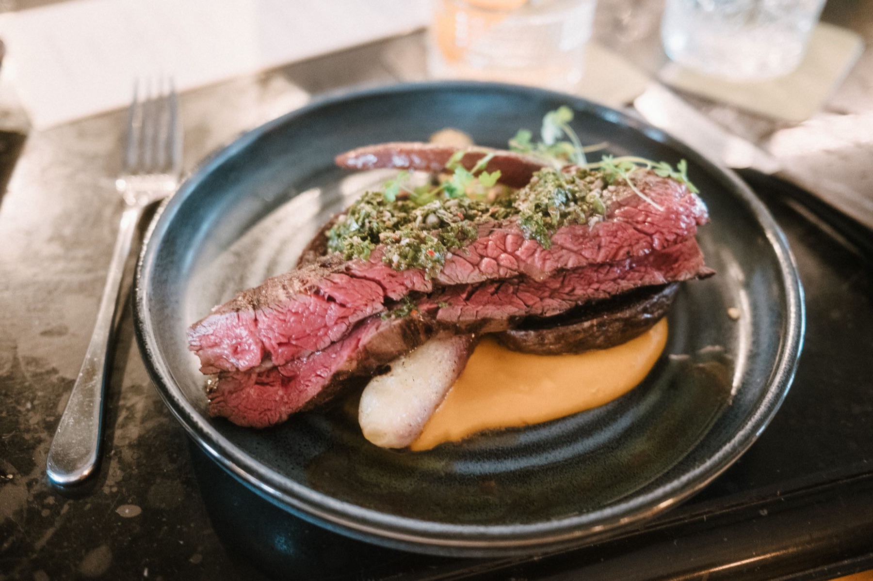 Gesneden bavette, rosé gebakken, met chimichurri en pompoencrème op een donker bord